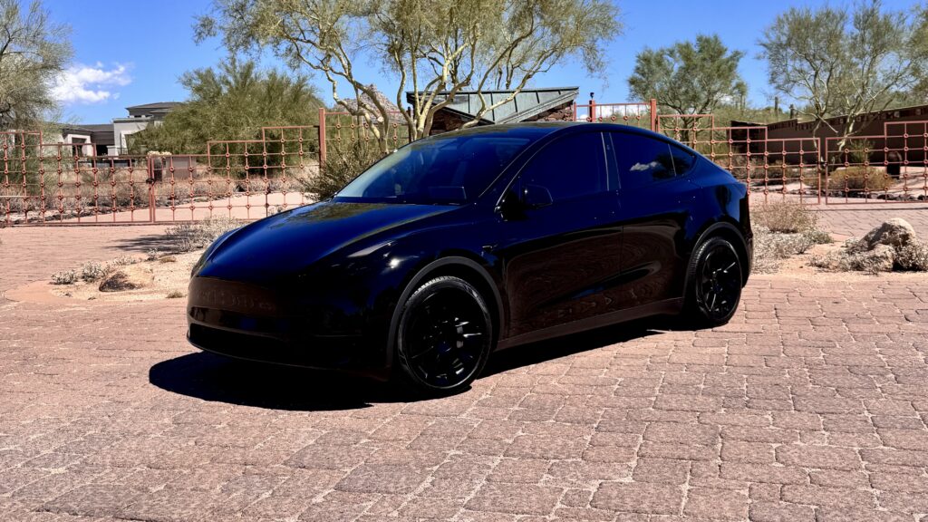 2025 Tesla Model Y rental car in black-on-black with black rims and tinted lights, parked in Scottsdale, AZ.